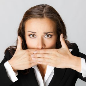 Portrait of surprised excited young businesswoman covering with hands her mouth, against grey background
